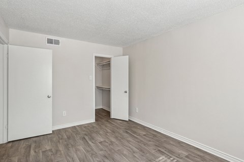 A white bedroom with a closet and wooden floors at The Park on Preston in Dallas, TX