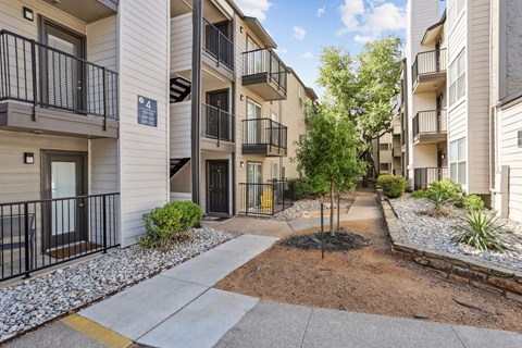 A paved path and landscaping between apartment buildings at The Park on Preston in Dallas, TX
