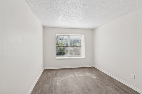 A white bedroom with a window and wooden flooring at The Park on Preston in Dallas, TX
