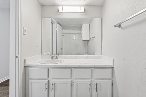 A bathroom with a white sink, mirror, and cabinets at The Park on Preston in Dallas, TX