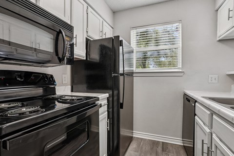 A kitchen with a black refrigerator, stove, and microwave at The Park on Preston in Dallas, TX