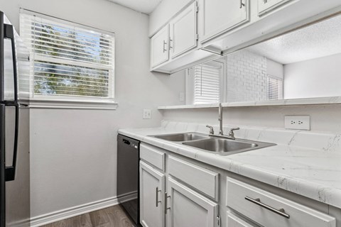 A kitchen with white cabinets and a black dishwasher at The Park on Preston in Dallas, TX