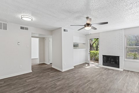 A spacious white living room with a fireplace and a ceiling fan at The Park on Preston in Dallas, TX