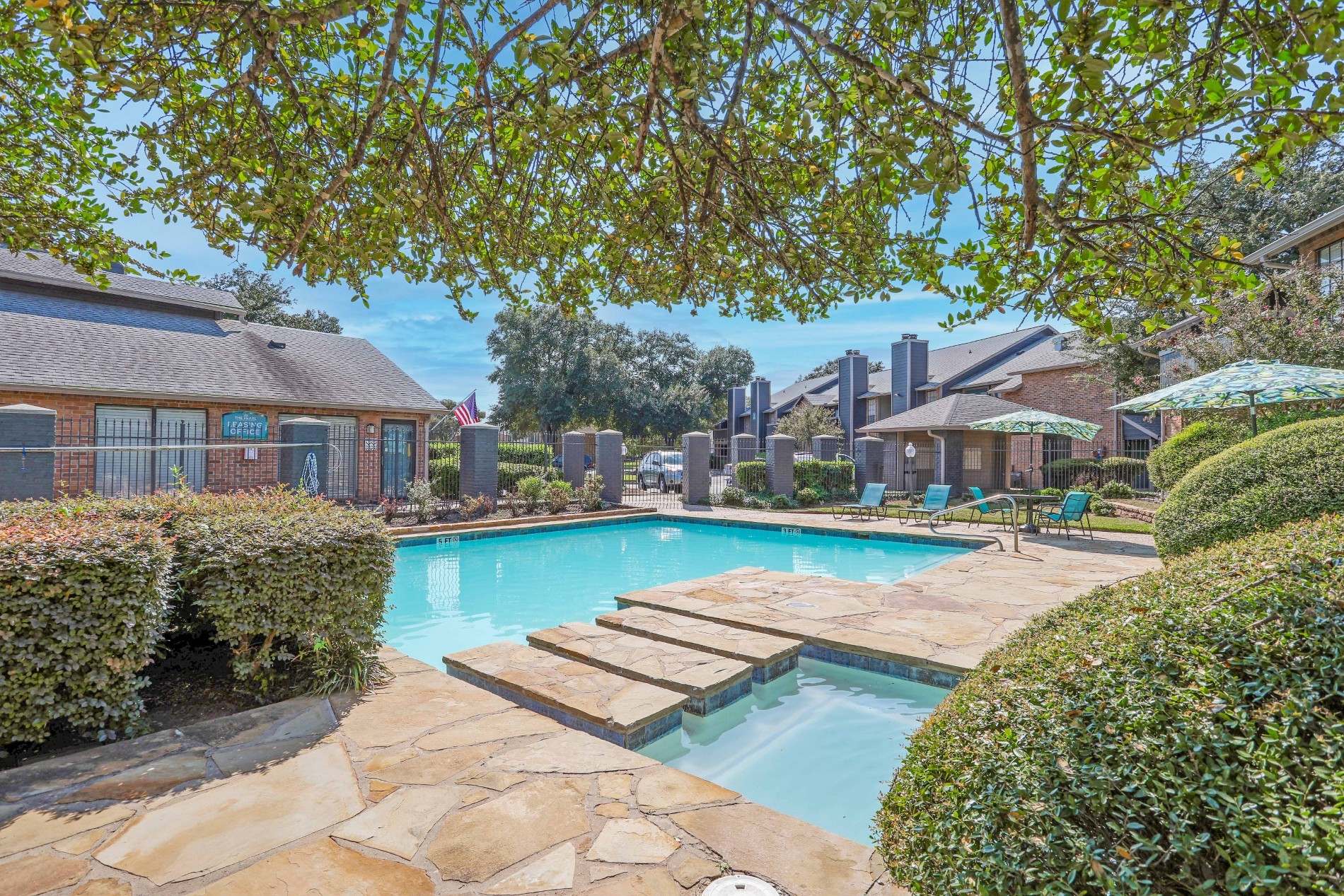 A swimming pool surrounded by a stone patio and green bushes.