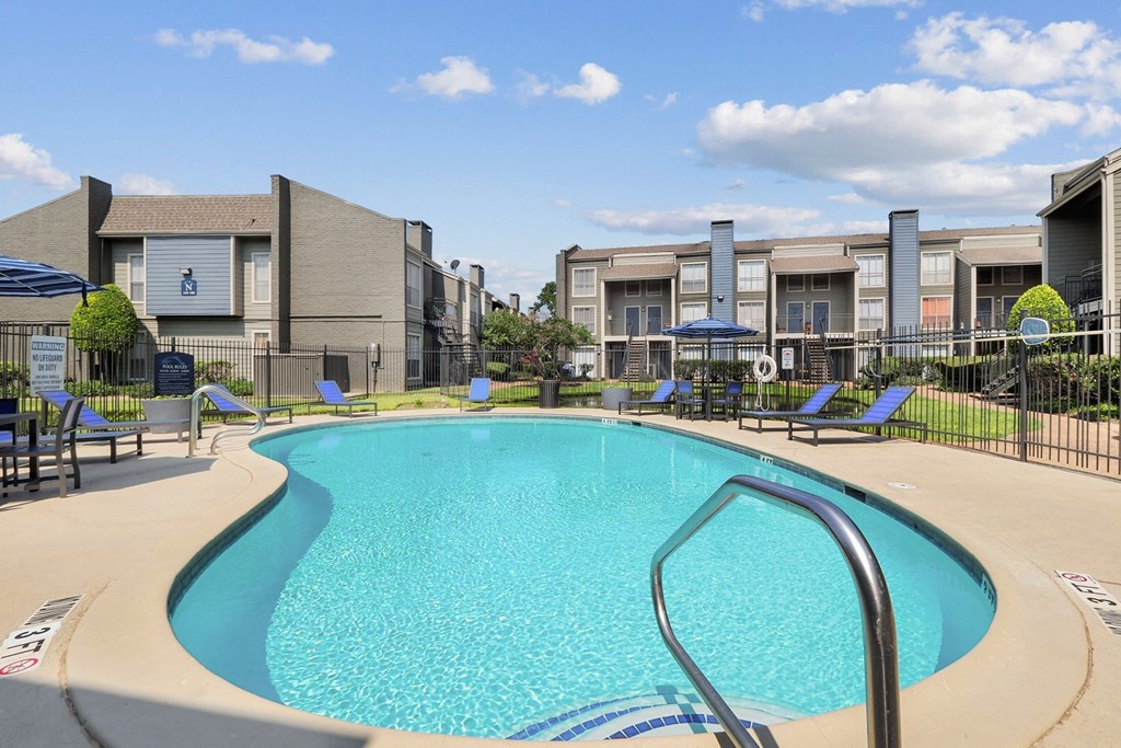 a swimming pool with lounge chairs and umbrellas with apartment buildings in the background