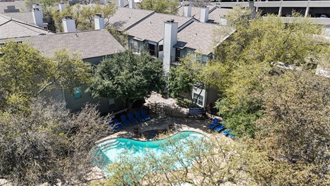 A swimming pool surrounded by lush trees and apartment buildings at The Park on Preston Apartments in Dallas, TX