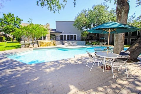 a swimming pool and patio with chairs and umbrellas