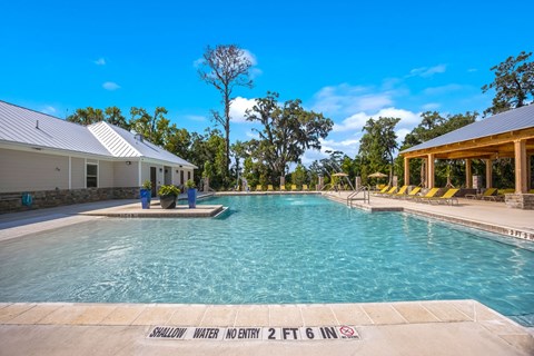 a large swimming pool with yellow lounge chairs and a white building in the background