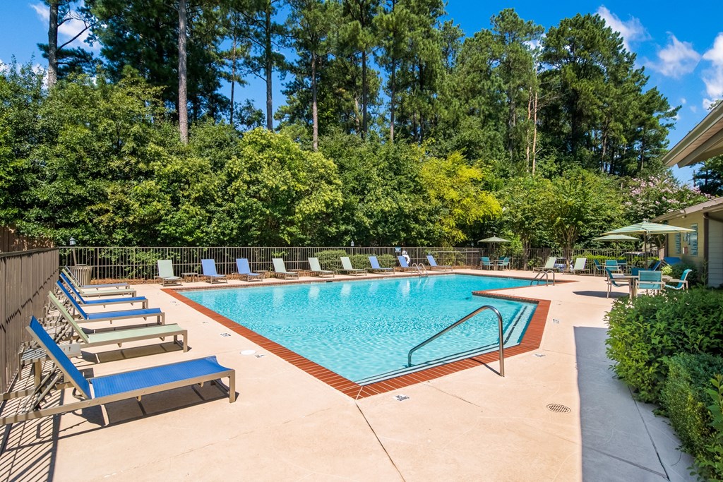 a swimming pool with chairs and trees in the background
