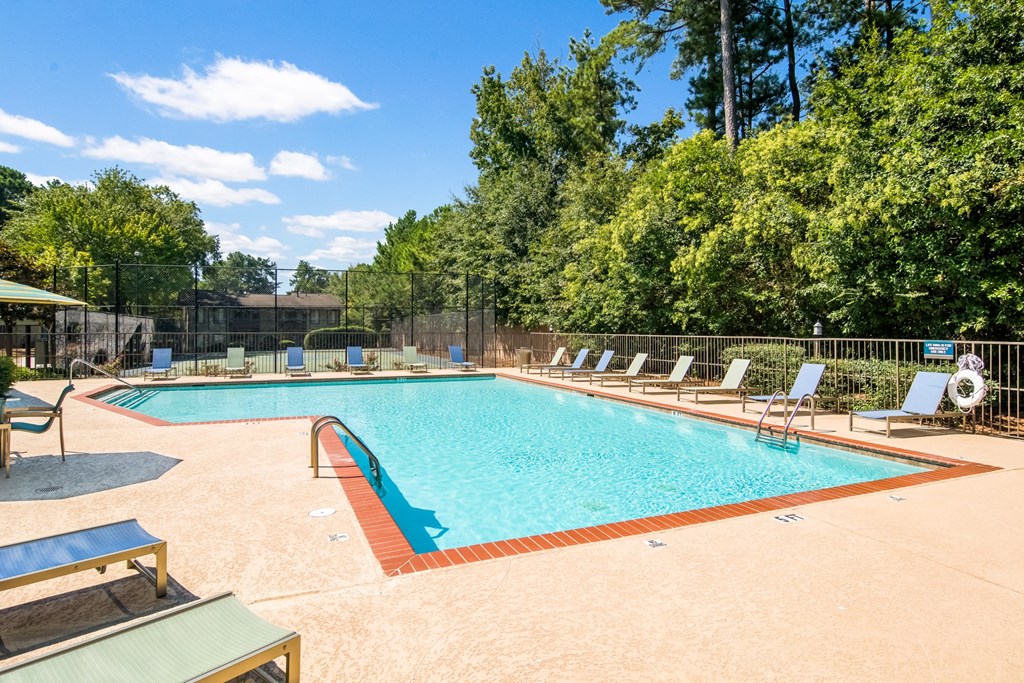 a swimming pool with chairs and trees in the background
