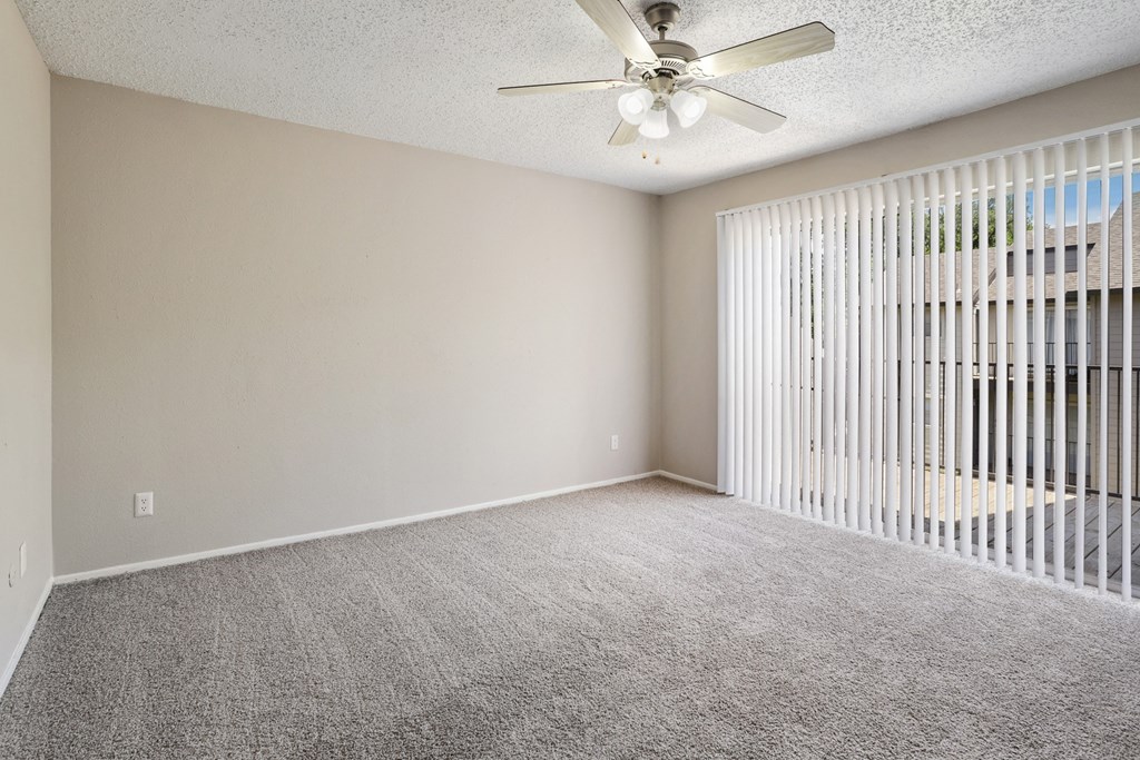 an empty bedroom with a ceiling fan and blinds