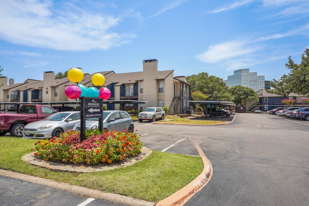 a parking lot with cars in front of a building with a sign with balloons