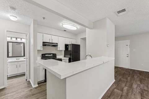 A white kitchen with a black refrigerator and wooden floors.