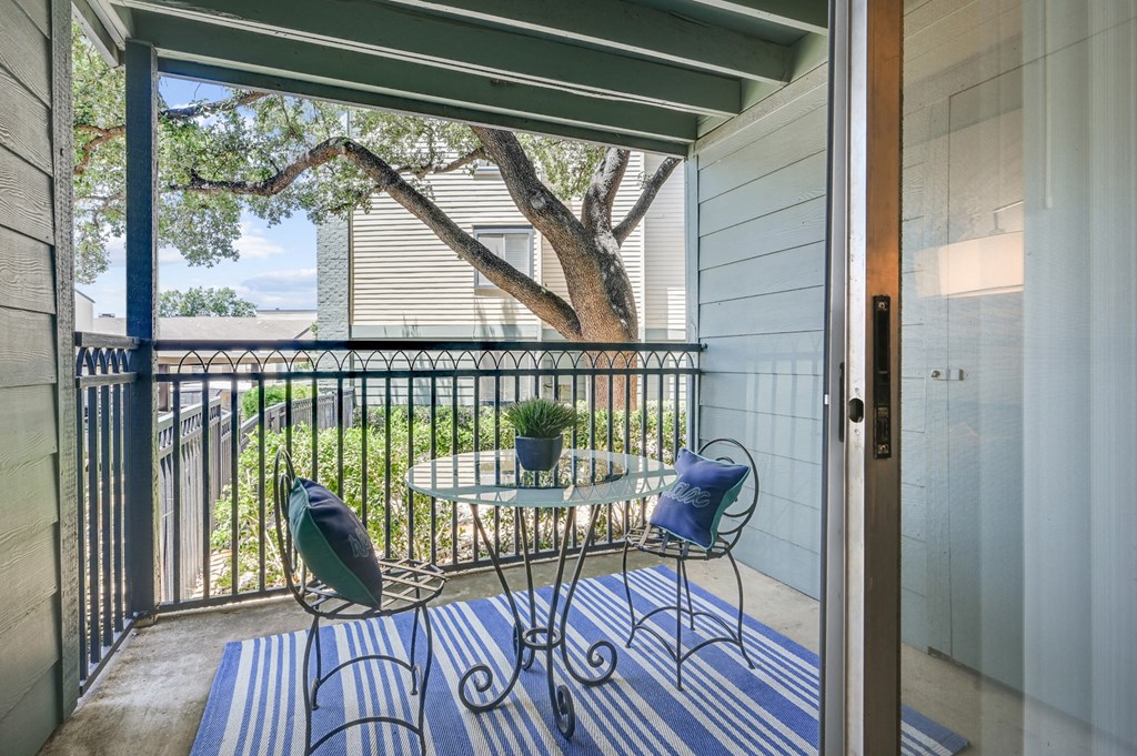 a small table and two chairs sit on a striped rug on a balcony with a sliding glass