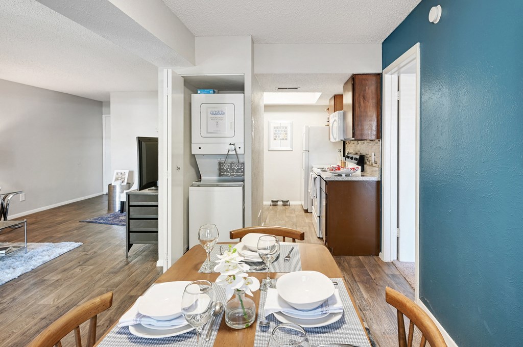 a dining area with a wooden table and chairs and a kitchen in the background