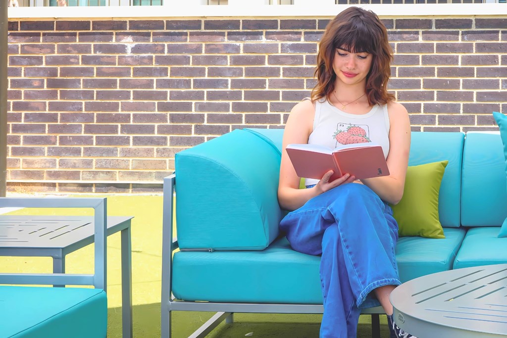 A woman is sitting on a blue couch reading a book at Era Apartments in Denton, TX