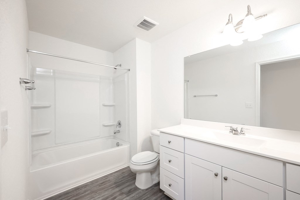 a bathroom with white cabinets and a white toilet next to a white bathtub at Beacon at Meridian, San Antonio