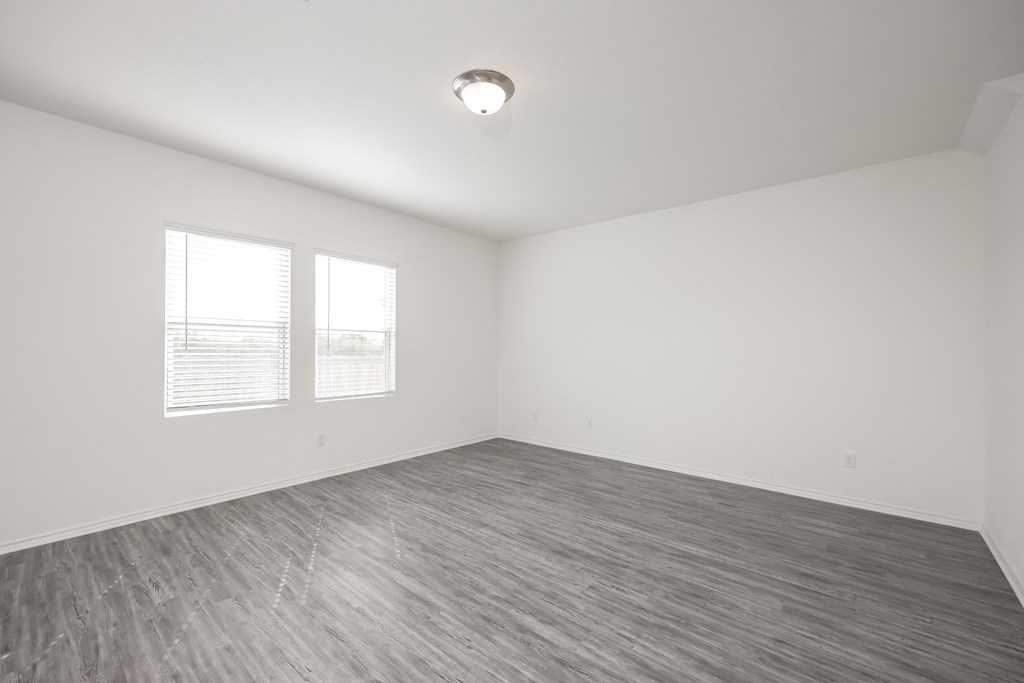 an empty bedroom with two windows and a hardwood floor at Beacon at Meridian, San Antonio, TX