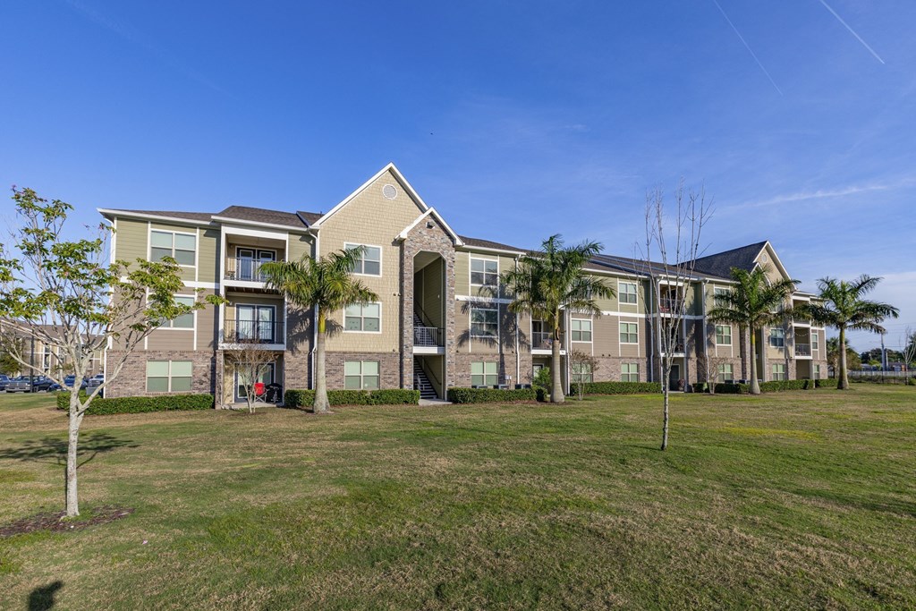 a row of apartment buildings with green grass and palm trees
