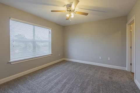 an empty living room with a large window and a ceiling fan