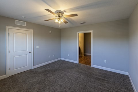 an empty living room with a ceiling fan and a door to a hallway