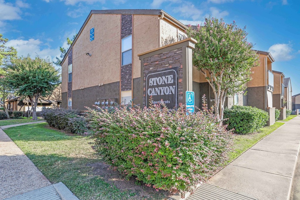 Property signage in front of apartment buildings and lush landscaping at Stone Canyon apartments in Shreveport, LA.