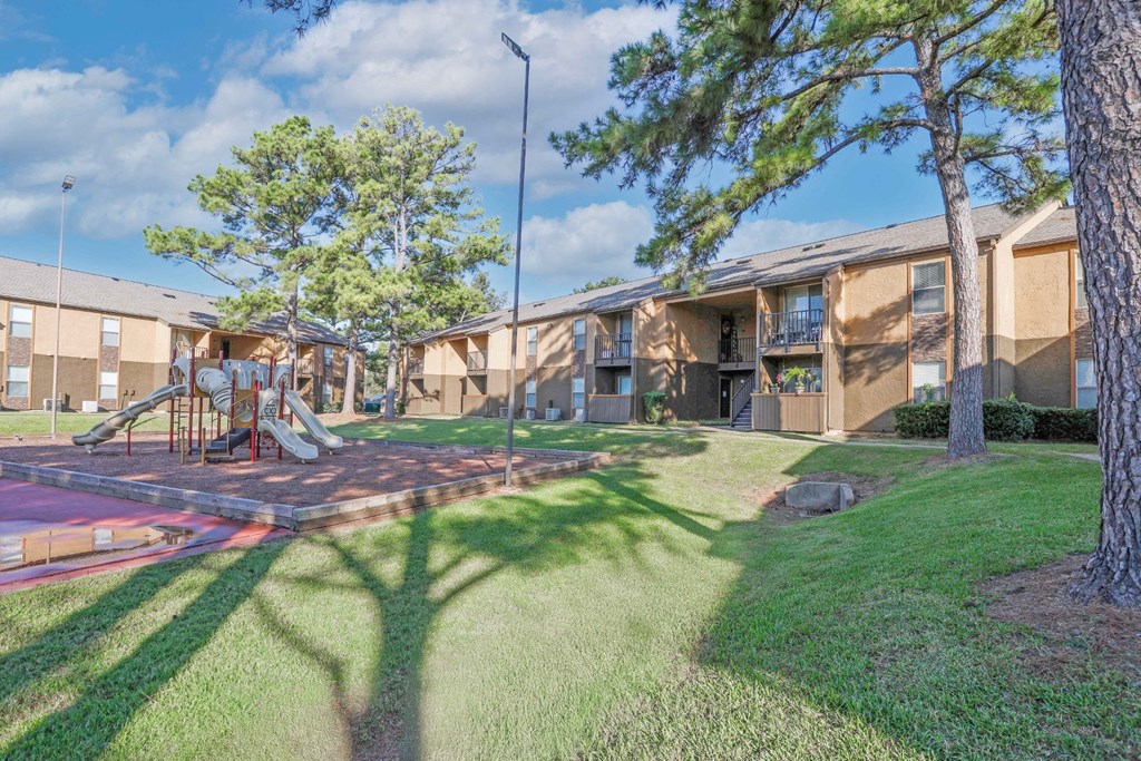 A playground with a slide and a tree in front of apartment buildings at Stone Canyon apartments in Shreveport, LA.