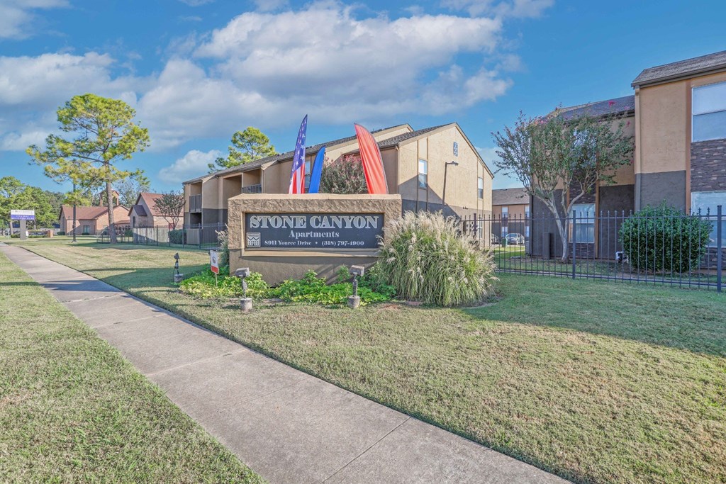 Stone Canyon Apartments signage with beautiful landscaping and apartment buildings behind at Stone Canyon apartments in Shreveport, LA.