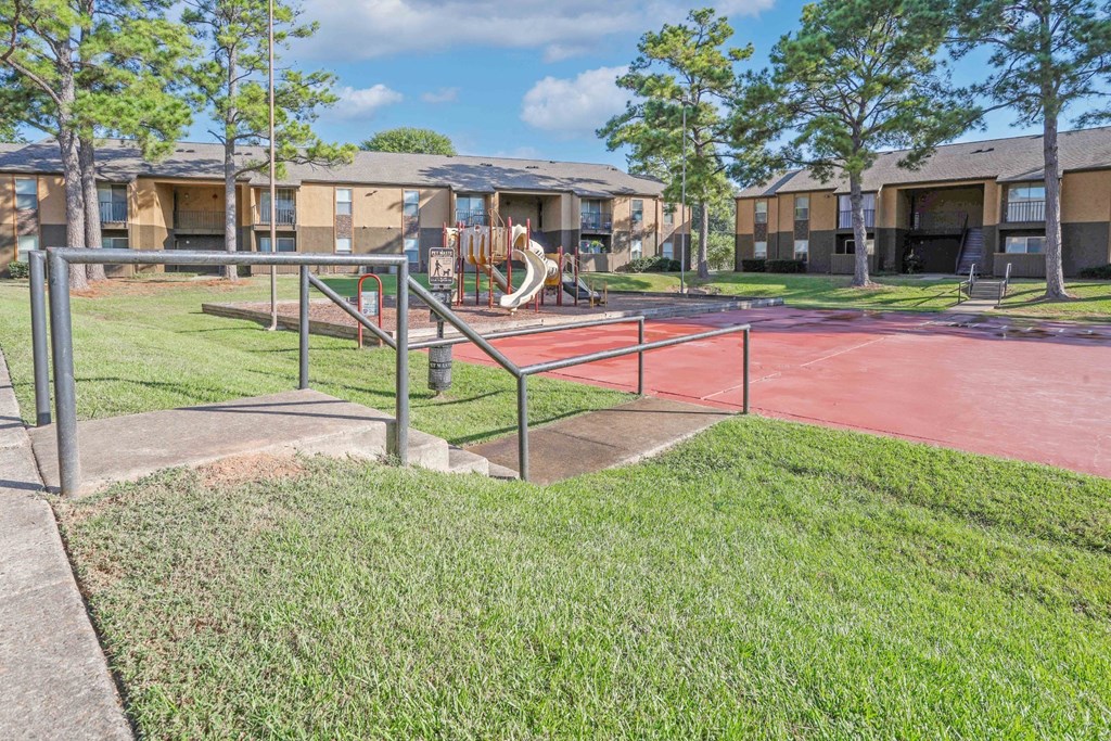 A playground with a red surface and a slide at Stone Canyon apartments in Shreveport, LA.