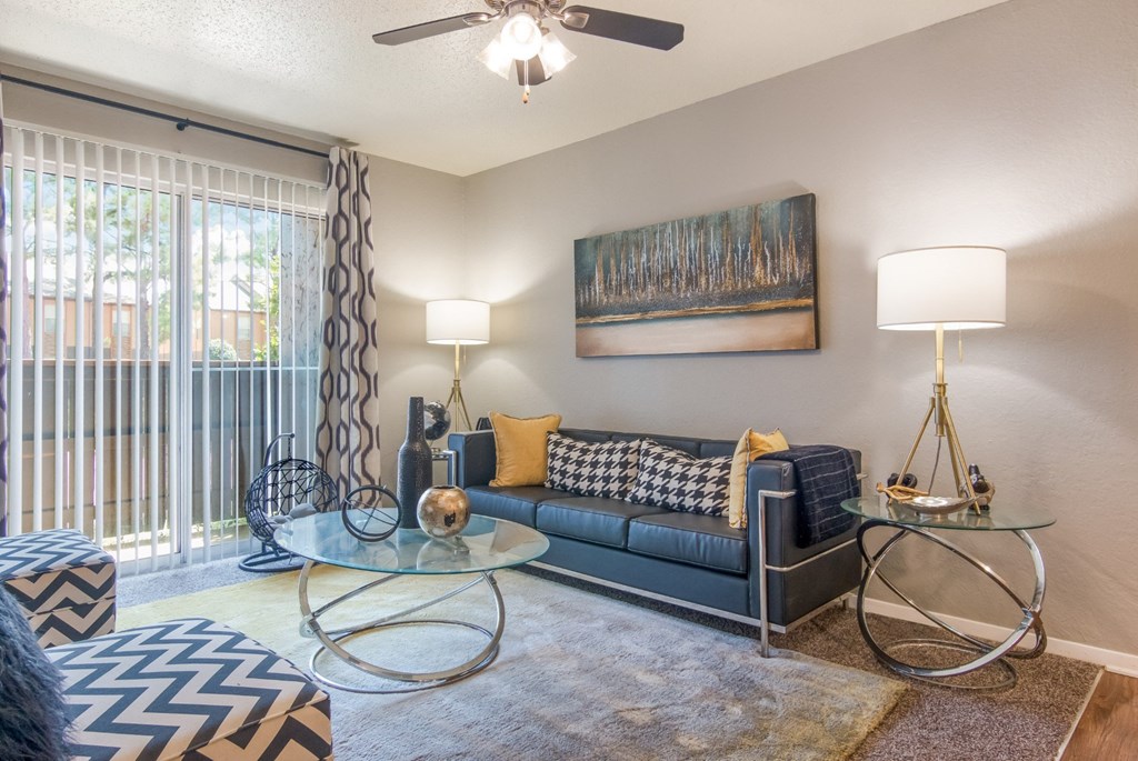 Model living room with a grey couch, a glass coffee table, and a ceiling fan at Stone Canyon apartments in Shreveport, LA.