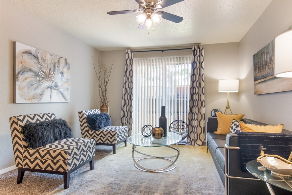 A living room with a patterned chair, a glass coffee table, and couch in the model apartment at Stone Canyon apartments in Shreveport, LA.