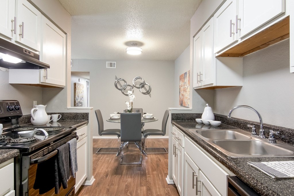 Model kitchen with a black stove top oven and white cabinets with view to dining area at Stone Canyon apartments in Shreveport, LA.