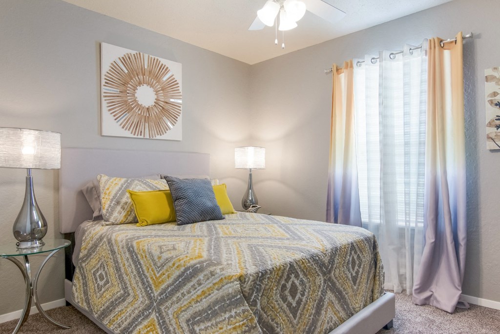 A bedroom with a bed, two lamps, and a decorative piece on the wall in the model apartment at Stone Canyon apartments in Shreveport, LA.