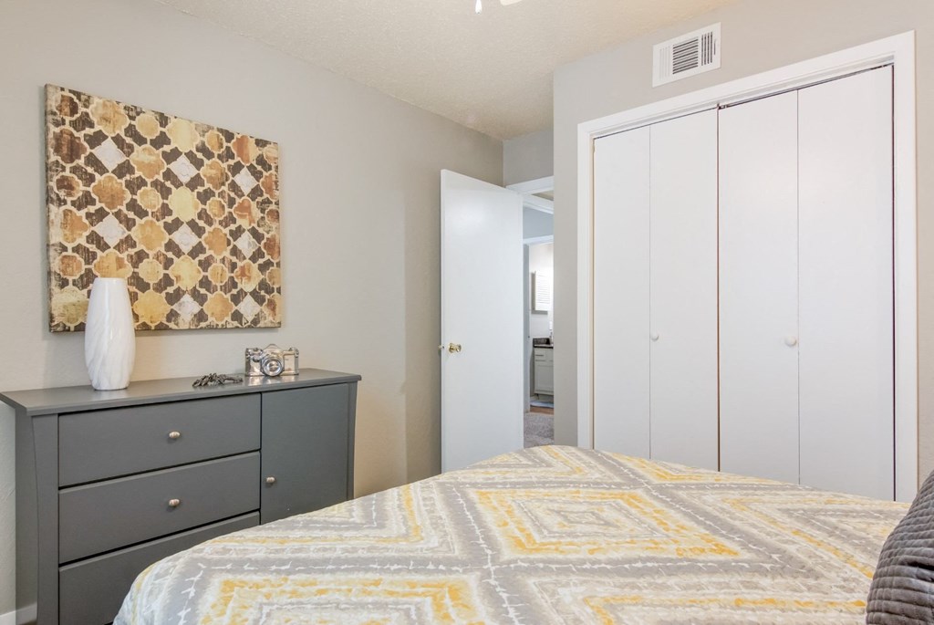 A bedroom with a bed, dresser, and a painting on the wall in the model apartment at Stone Canyon apartments in Shreveport, LA.