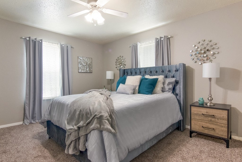 A bedroom with a large bed and a ceiling fan in the model apartment at Stone Canyon apartments in Shreveport, LA.