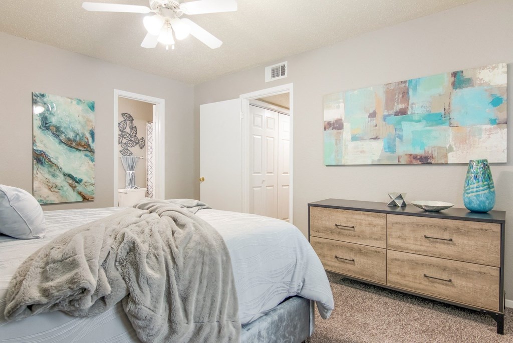 A bedroom with a bed, a ceiling fan, and a painting on the wall in the model at Stone Canyon apartments in Shreveport, LA.