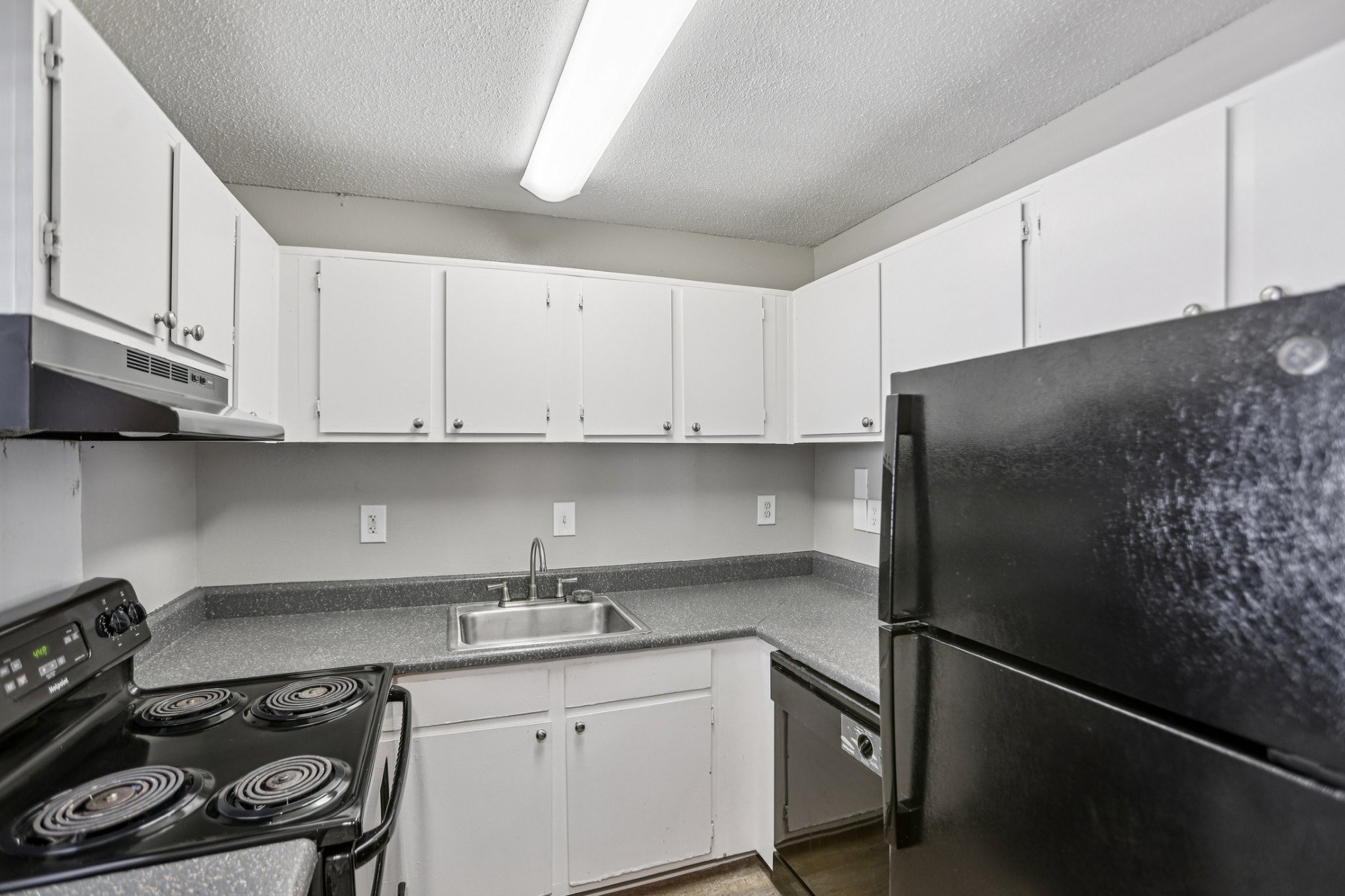 A black refrigerator is in the corner of a kitchen with white cabinets.