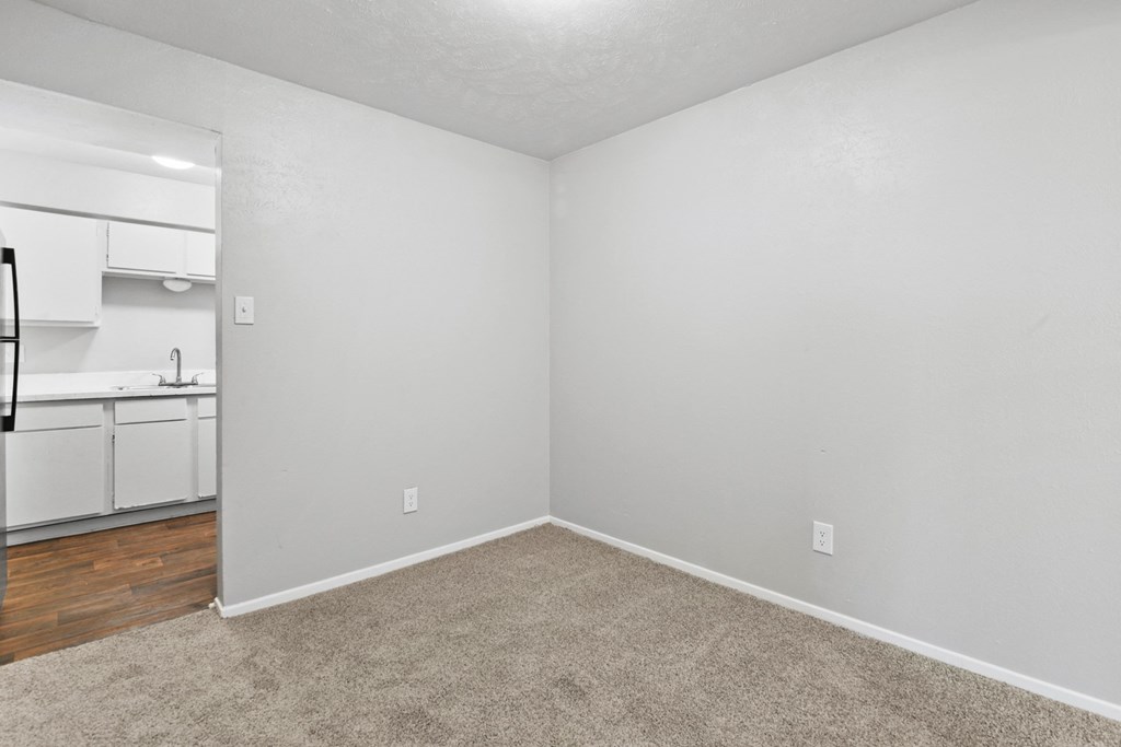 an empty bedroom with a kitchen in the background