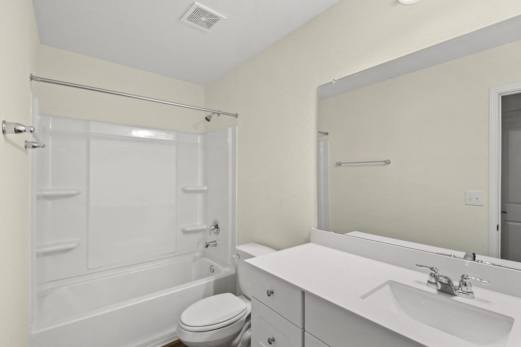 a bathroom with a shower bathtub, big mirror and white cabinets