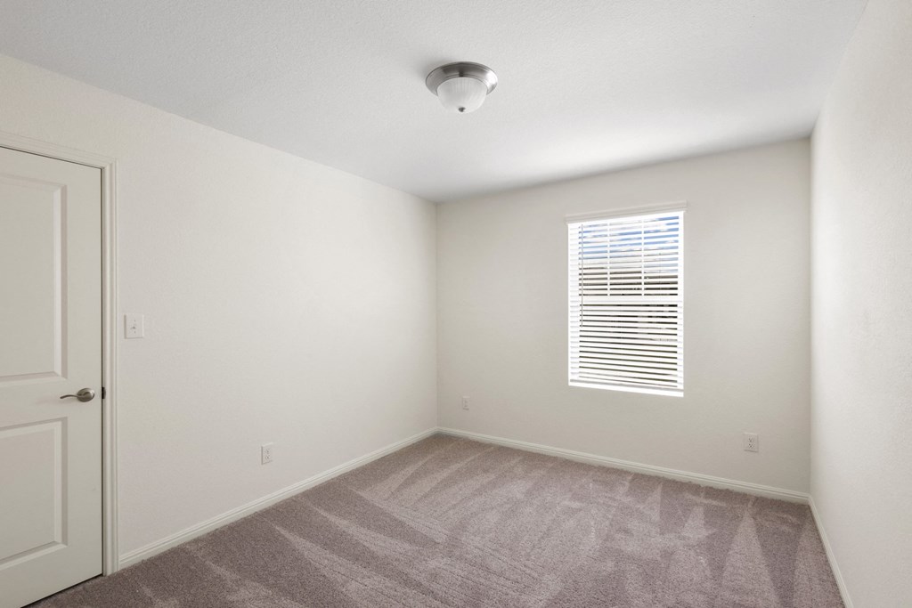 a bedroom with a window, white walls and carpet