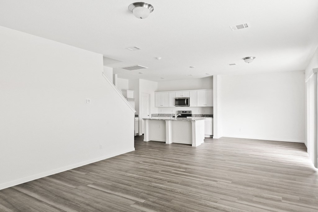 a spacious family living room and kitchen with white walls and wood floors