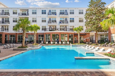 A large swimming pool in front of a multi-story apartment building at The Grand At Upper Kirby in Houston, TX