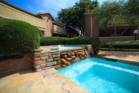 a swimming pool with a stone retaining wall and a spa in front of a house