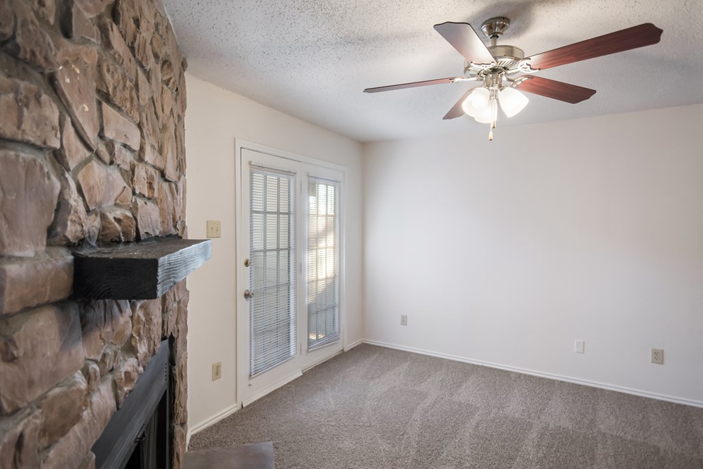 an empty living room with a stone fireplace and a ceiling fan