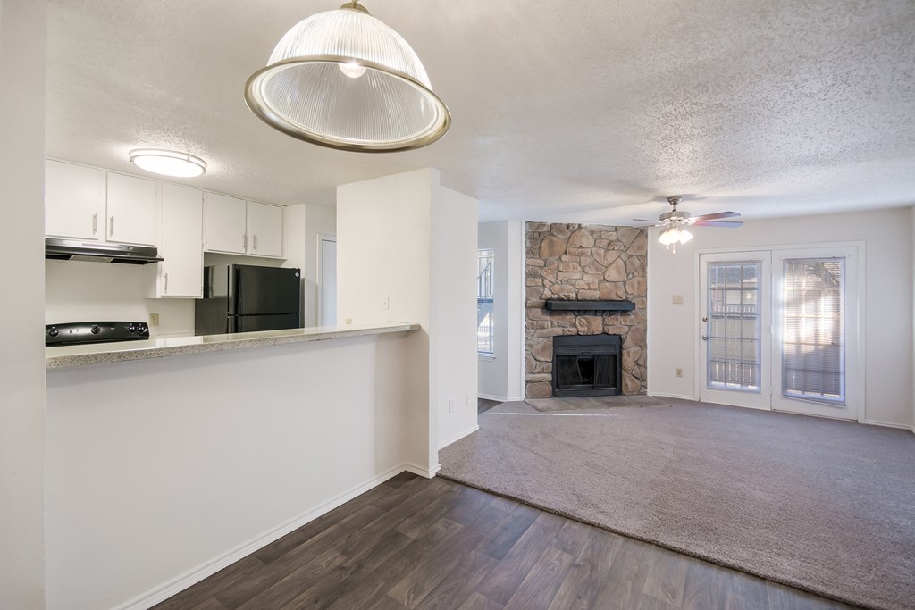 an empty living room and kitchen with a stone fireplace