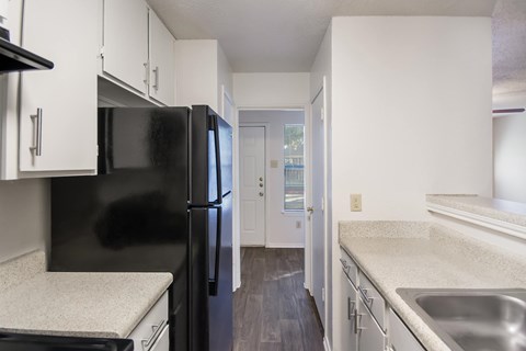 A black refrigerator in a kitchen with white cabinets.