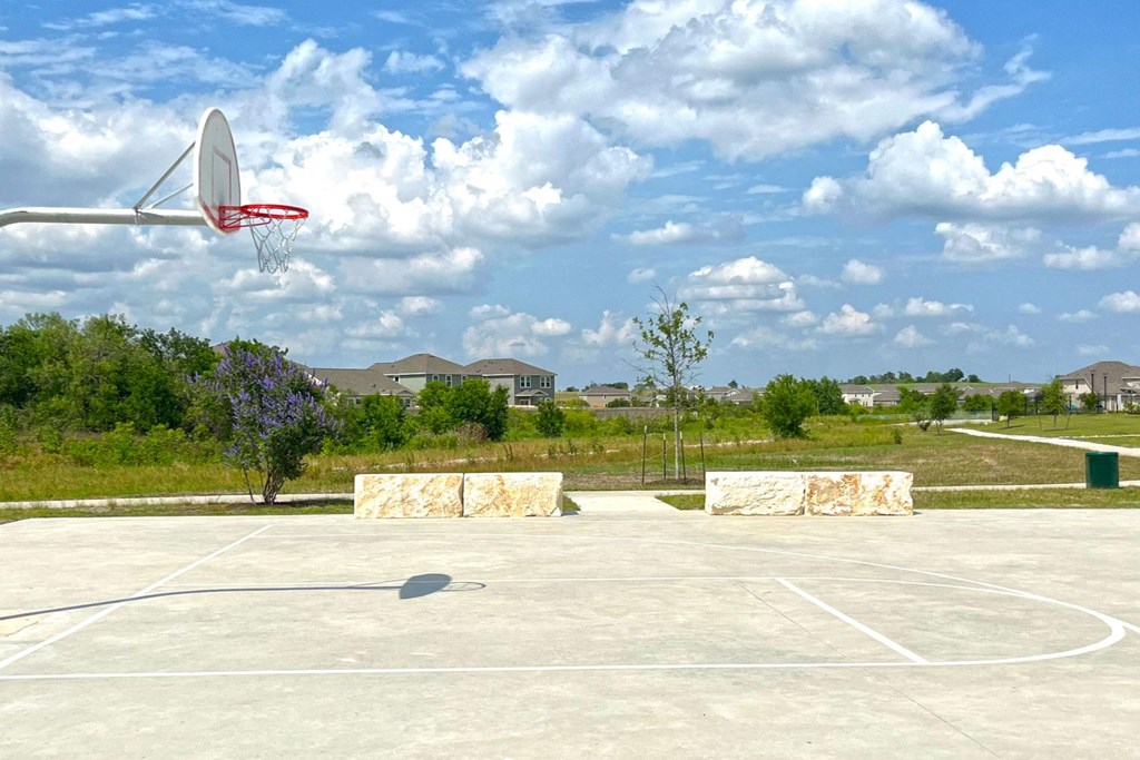 a basketball court in a park with houses in the background at Beacon at Vine Creek, Pflugerville, Texas