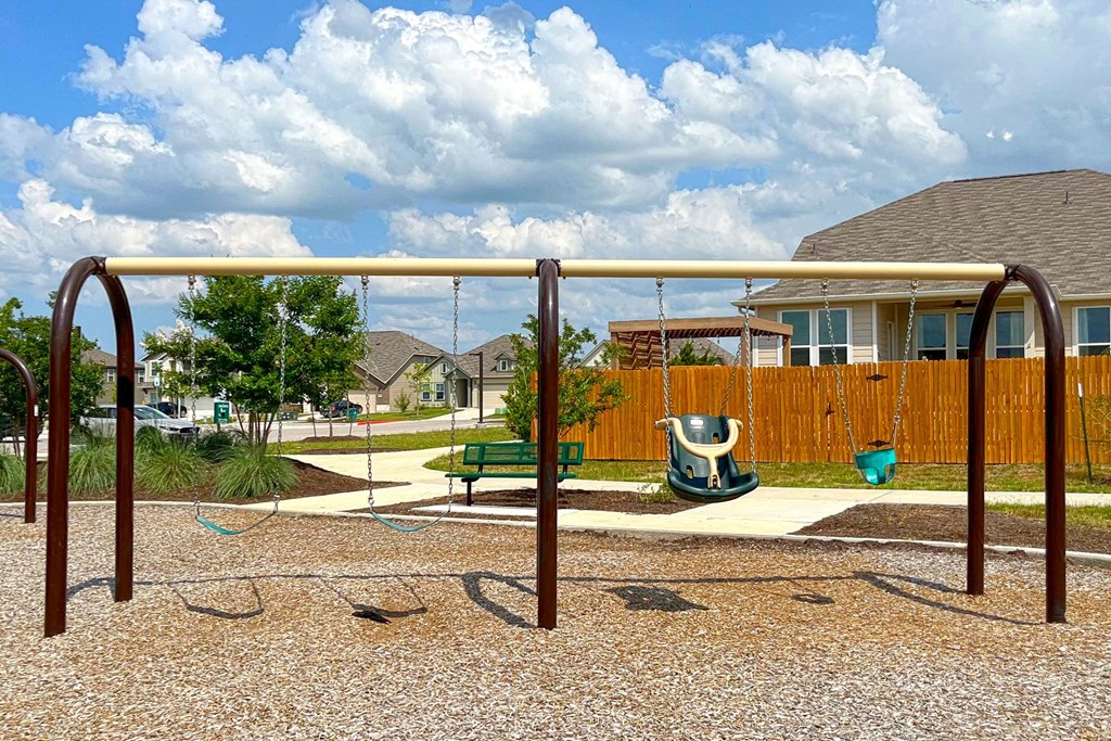 a swing set in a park with a house in the background at Beacon at Vine Creek, Pflugerville, TX