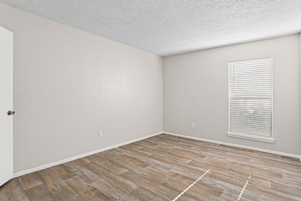 A1 bedroom with wooden flooring and a window with blinds at Vine Apartments in Arlington, TX