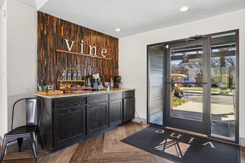 A coffee bar area with a wooden backdrop and a chair in front of it in the lobby of Vine Apartments in Arlington, TX